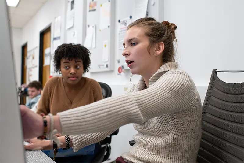 Two women in discussion and gesturing towards computer display