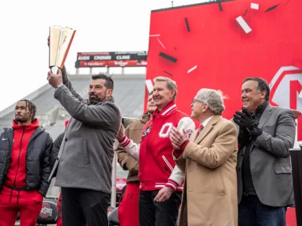 Coach Ryan Day lifts the national championship trophy as Univeristy President Ted Carter pats his shoulder and Ohio's governor and Columbus' mayor clap