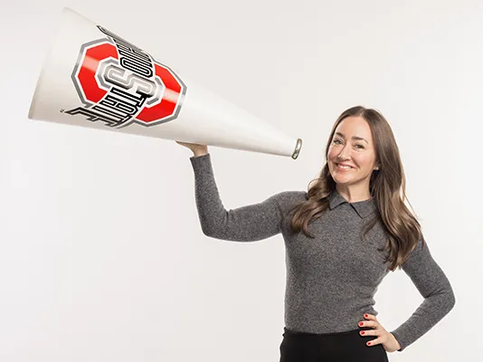 A pretty white woman with long hair and a friendly smile holds up a megaphone she used while a cheerleader in her Ohio State days